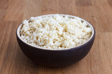 Cooked quinoa in a ceramic bowl on wood table.
