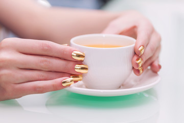 Female hands with elegant gold manicure hold a cup of tea