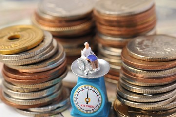 お金に囲まれて計りに乗せられている車椅子の高齢者