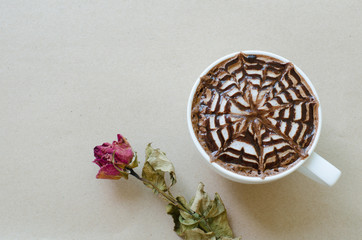 A cup of coffee with latte art and wither rose on brown paper ba