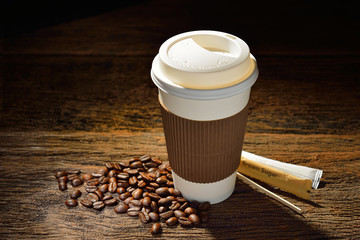 Paper cup of coffee and coffee beans on wooden table