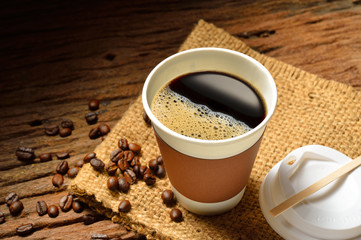 Paper cup of coffee and coffee beans on wooden table