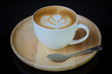 a cup of latte art on wooden plate