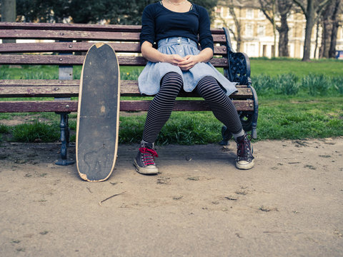 Woman with skateboard sitting on park bench