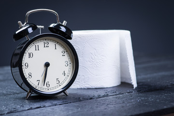 Alarm clock with toilet paper on a black wooden table