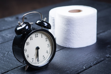 Alarm clock with toilet paper on a black wooden table