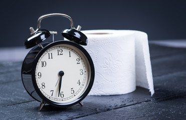 Alarm clock with toilet paper on a black wooden table