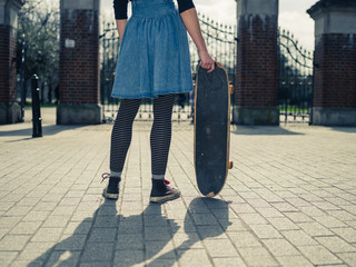 Young woman standing at gates of park with skateboard