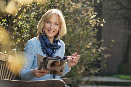 smiling mature woman is reading a magazine
