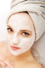 Woman relaxing in bathtub with face mask.