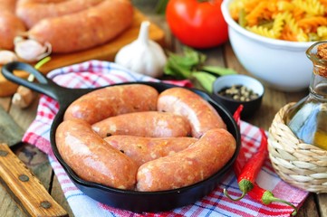 raw chicken sausages with vegetables on a frying pan