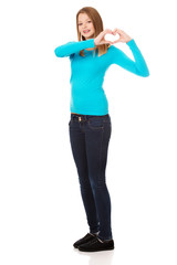 Fototapeta premium Smiling teenage woman making heart shape