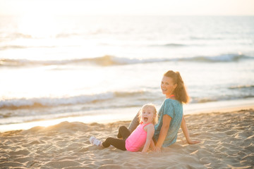 Fototapeta na wymiar Healthy mother and baby girl sitting on beach in the evening