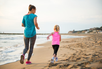 Healthy mother and baby girl running on beach. rear view