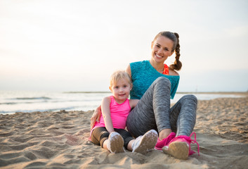 Happy healthy mother and baby girl sitting on beach