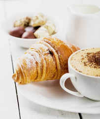 Hot cappuccino and pastries on white wooden boards