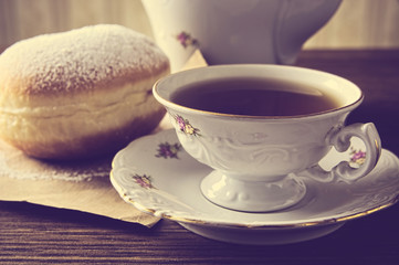 Closeup shot of donut with cup of tea on table in old-fashioned