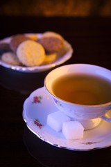 Old-style image cup of tea with cookies on black