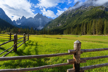 Fototapeta na wymiar Fence on green pasture in Dolomites Mountains in summer, Italy
