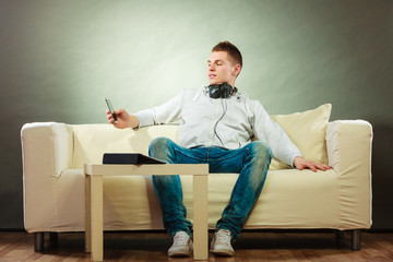 man on couch with headphones smartphone and tablet