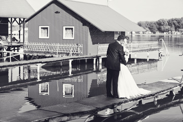 Bride and groom holding each other on bridge near lake house