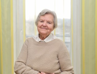 Senior happy woman in her home with window on background.