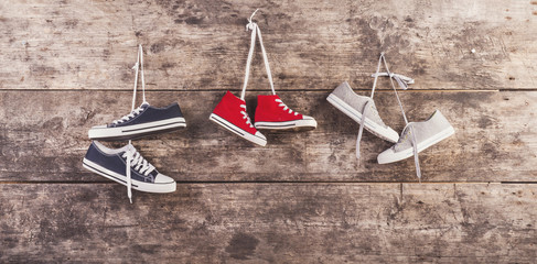 Three pairs of sneakers hang on nail on wooden fence background