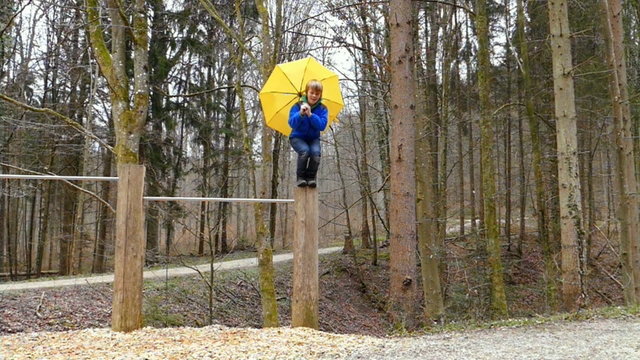 Kind springt von einem Stamm herunter mit Regenschirm, Zeitlupe