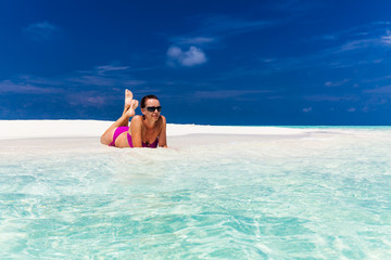 Young woman in purple bikini relaxing on sand on tropical beach