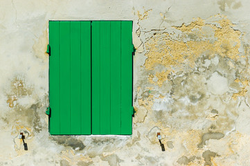 A closed green shutter and an old concrete wall illuminated by a strong sun light