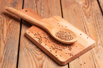 Dry buckwheat in a spoon on a wooden cutting board
