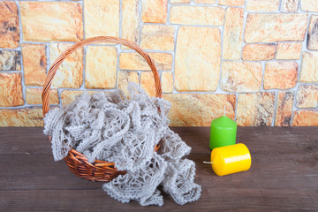 Knitted scarf in the basket and two color candles on wooden tabl