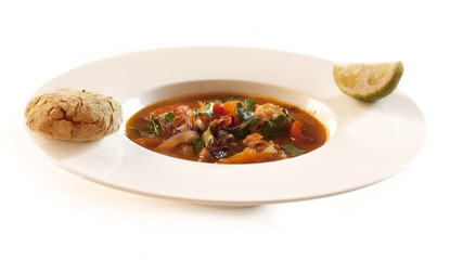 Homemade tomato seafood soup with bun and lime slice.