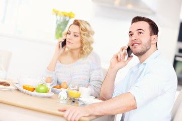 Obraz na płótnie Canvas Happy couple eating breakfast and using smart phone