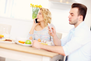 Obraz na płótnie Canvas Happy couple eating breakfast and using smart phone