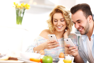 Happy couple eating breakfast and using smart phone