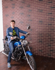 Obraz na płótnie Canvas Young Man on Blue Motorcycle by Brick Wall