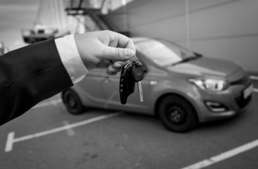 black and white photo of man in suit holding car keys against ne