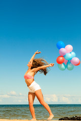 Girl jumping with colorful balloons on beach