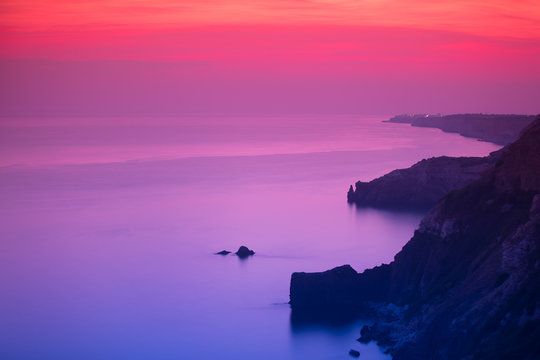 Purple And Pink Sunset Over Ocean Shore And Mountains