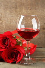 Composition with red wine in glass, red roses and decorative heart on wooden background
