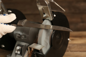 Knife sharpener and hand with blade on wooden table, closeup