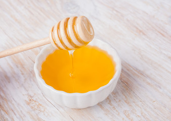 Honey with a stick in a white bowl on wooden table