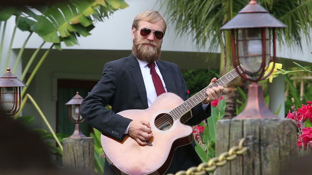 bearded man in black  stands in position to play guitar