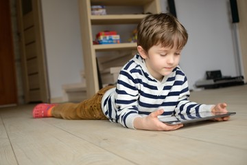 boy lying on the floor and uses his tablet