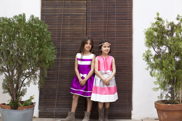 Niñas con vestidos de  fiesta junto a persiana de madera