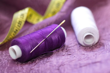 Needle and spools of thread on color textile - obrazy, fototapety, plakaty