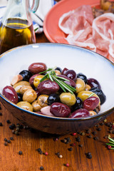 Olives in bow with prosciutto on wooden table