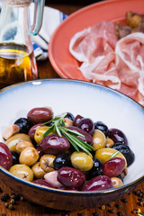 Olives in bow with prosciutto on wooden table