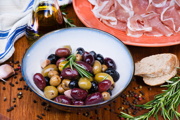 Olives in bow with prosciutto on wooden table